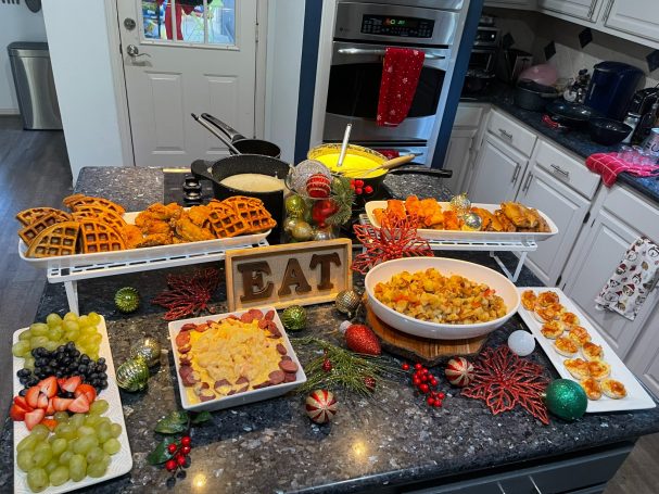 A festive spread of various dishes and fruits on a kitchen countertop with a "EAT" sign.